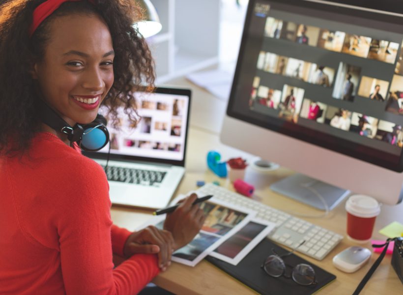 Portrait of young mixed-race female graphic designer looking and smiling at camera while working at desk in a modern office